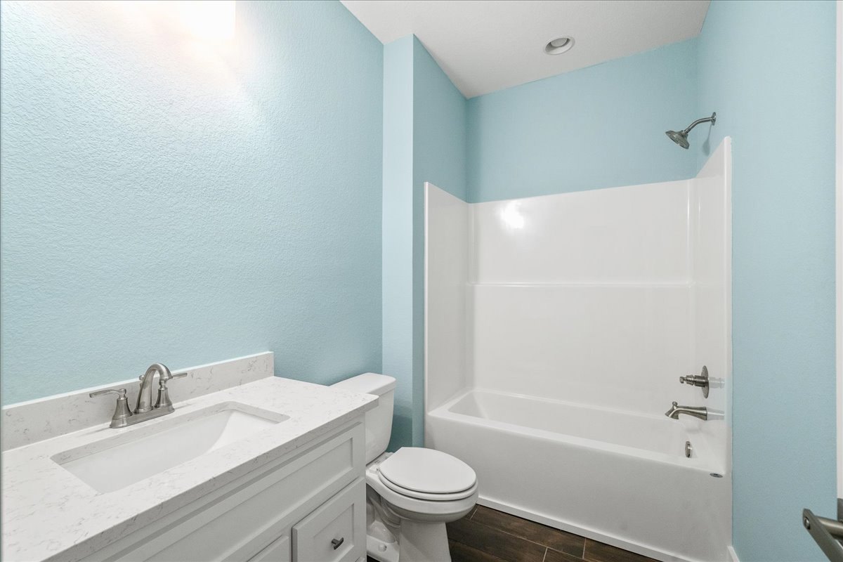 White freestanding bathtub beside a toilet, white sink with chrome faucet, tiled walls, shower head with water running, bathroom cabinet visible.