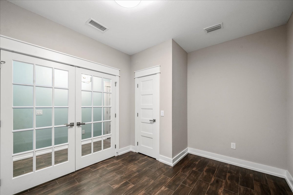 Double glass-paneled doors and single white door with silver handle, wood flooring with white trim, ceiling vent, white plastic tube on white surface
