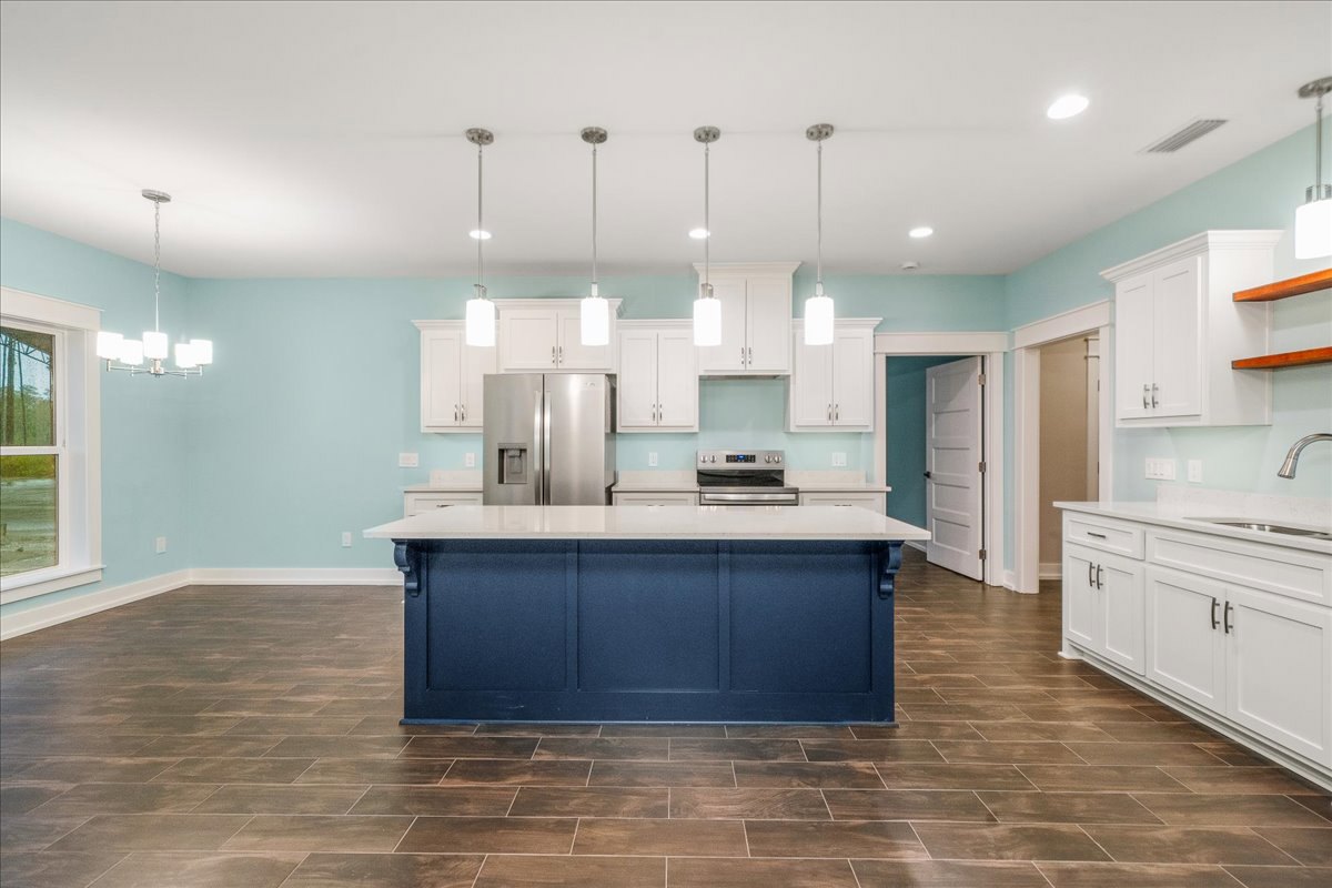 Kitchen with central island, stainless steel refrigerator and oven, blue accent wall with white trim, white door with black knob, white-framed window, tile flooring, white