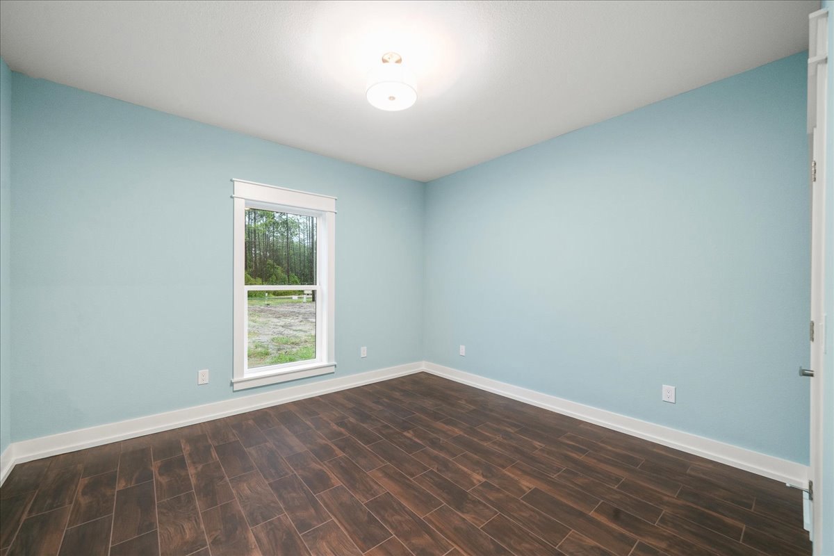 Sunlit room with wide window overlooking leafy trees, smooth wood flooring, white plaster walls, and modern ceiling light fixture