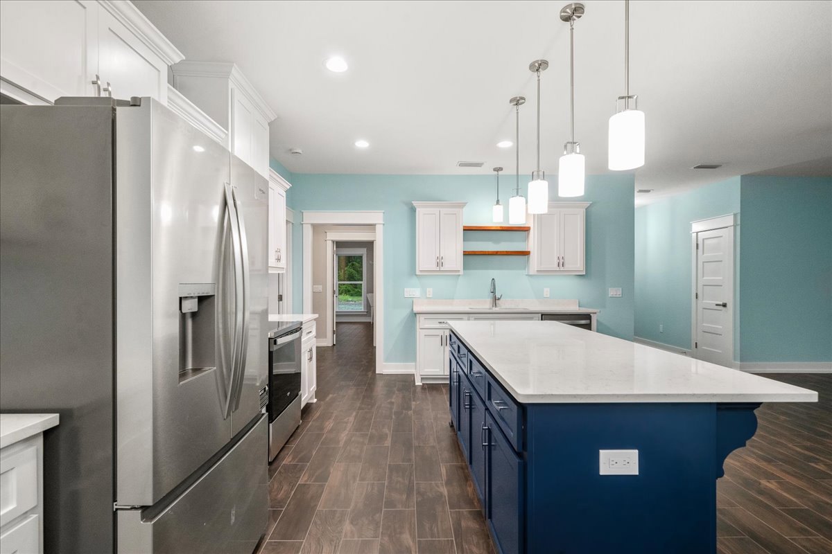 Spacious kitchen featuring a large central island with white countertop, stainless steel refrigerator, tile backsplash, white cabinetry, black hardware, and wood flooring