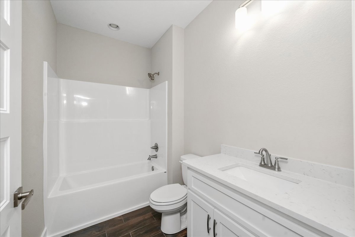 White porcelain sink with chrome faucet, matching toilet, white bathtub, light-colored tile walls, and modern bathroom accessories
