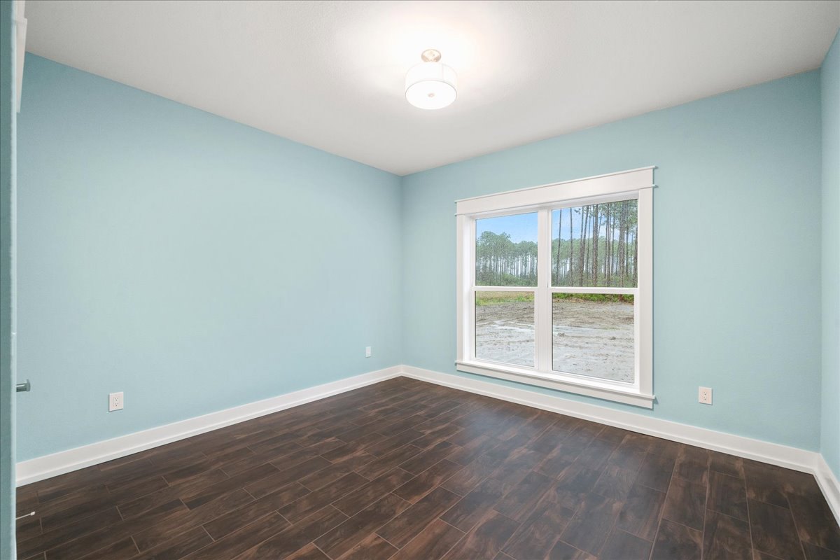 Spacious room with wide window overlooking forest, light wood flooring, white plaster walls, and modern ceiling light fixture