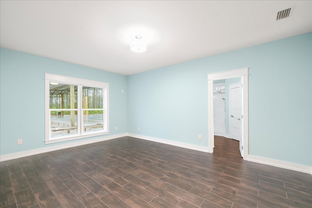 Wood floor room with blue accent wall, large window overlooking forest, white door with silver handle, bathroom shower, white ceiling light fixture.