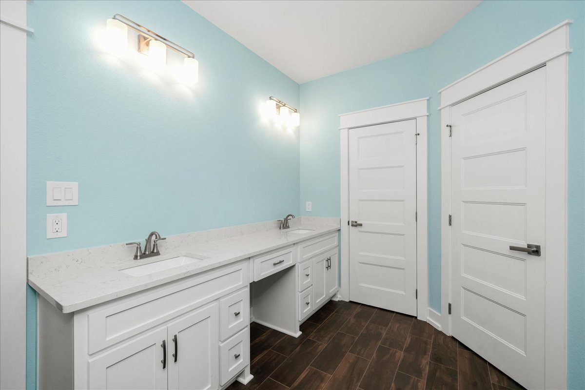 Bathroom with white cabinets, white doors with silver handles, brown tile floor with white trim, three-light fixture, rectangular light switch, and close-up of chrome faucet on