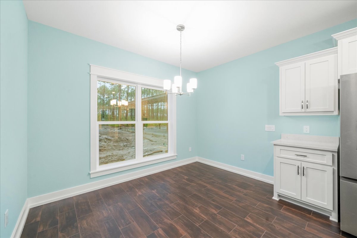 White shaker cabinets with silver handles, stainless steel sink beneath a window overlooking a dirt field, wood plank flooring, white walls, and black cabinet pulls.