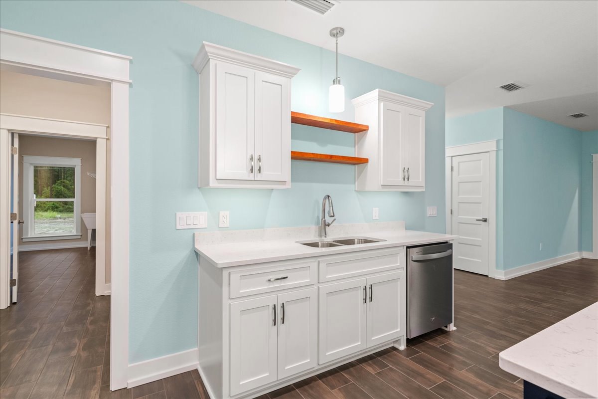 White kitchen cabinets with silver handles, white countertop, dark wood flooring, stainless steel dishwasher and refrigerator, window overlooking forest, white door with silver