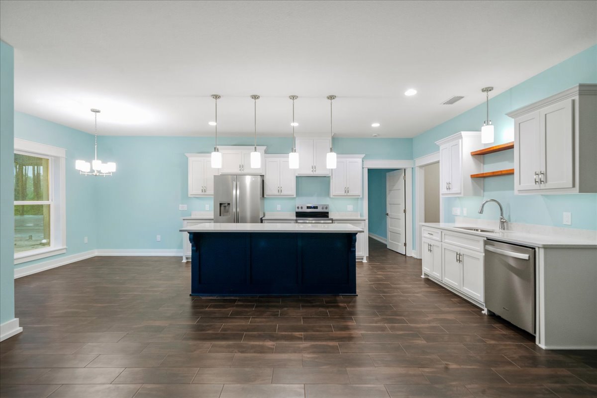 Blue and white kitchen island with quartz countertop, stainless steel refrigerator, white cabinetry, brown tile floor, and window with white trim; person standing beside