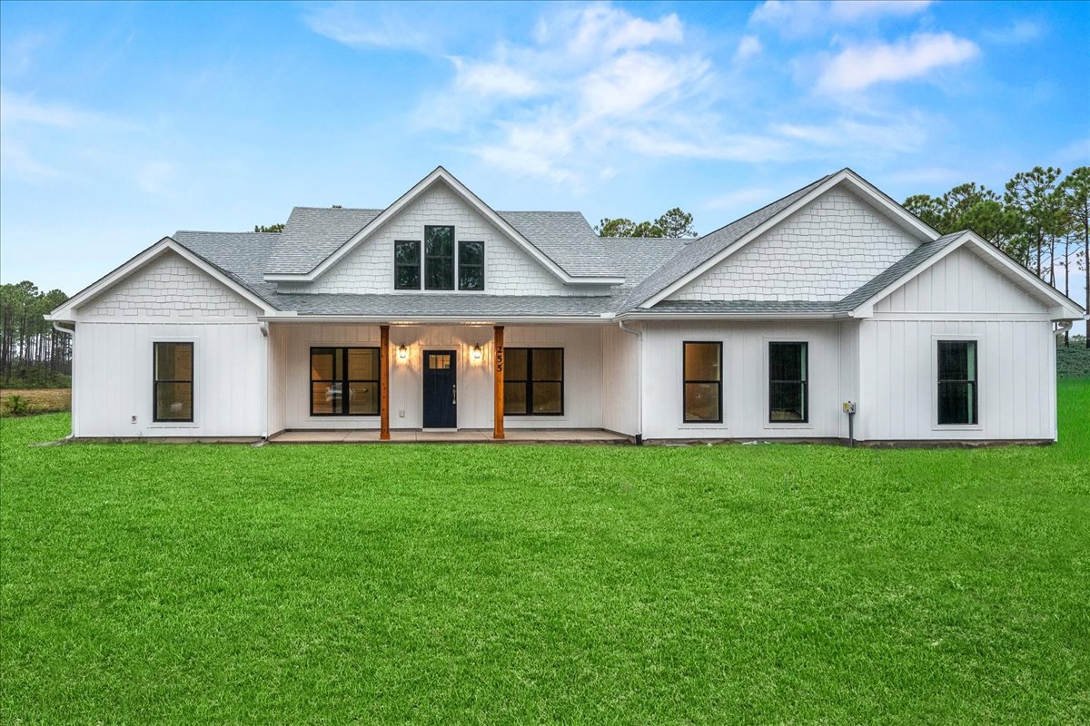 White house with blue door and black-framed windows, surrounded by green lawn, Robert Frost Farm visible in background under partly cloudy sky