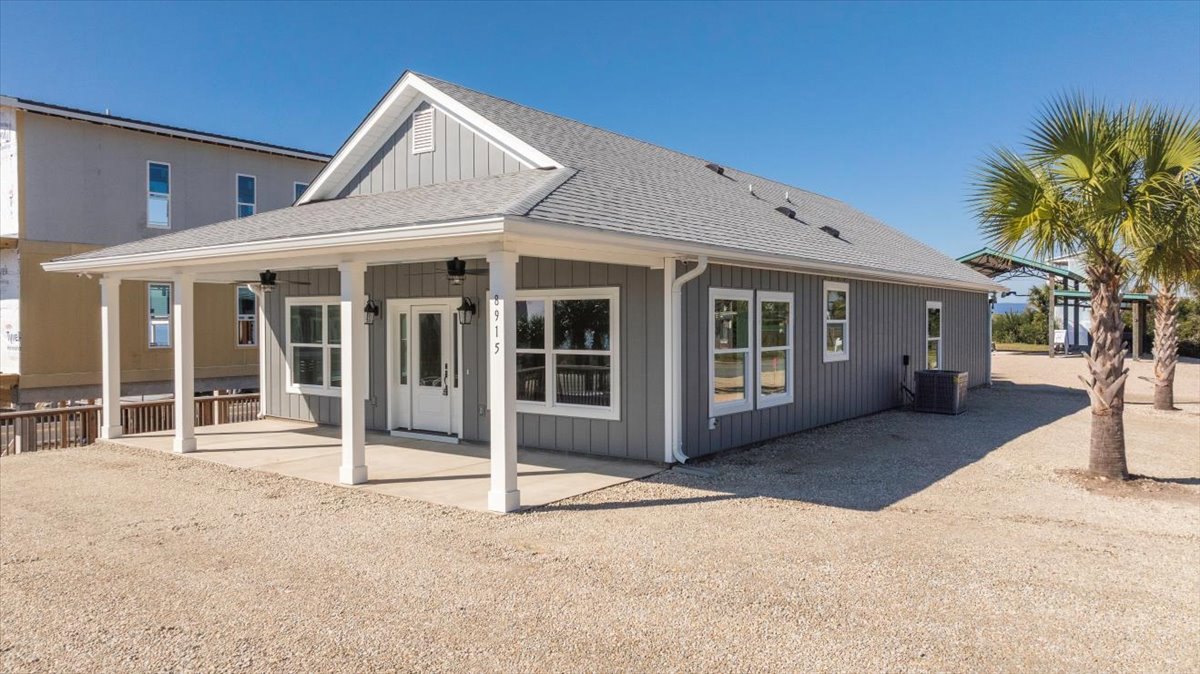 Gravel driveway leading to a custom home with white columns, palm trees, double glass doors, and large windows on the exterior porch.