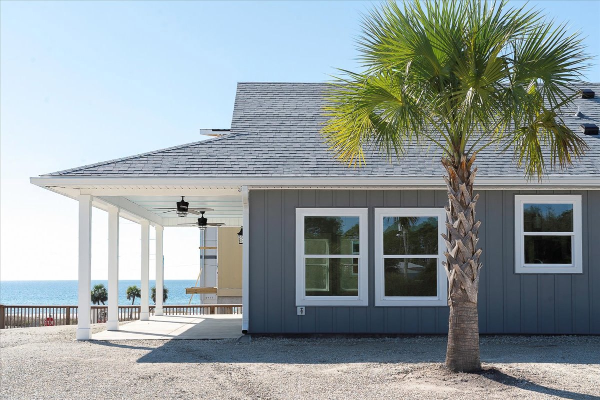 White-framed window and covered porch shaded by a tall palm tree, stucco exterior, blue sky above