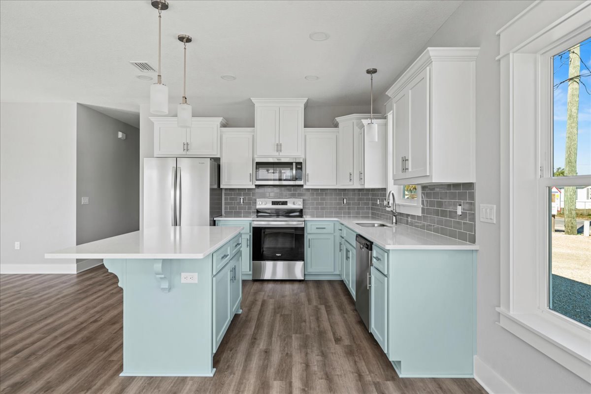 White kitchen cabinets, blue island with wood flooring, stainless oven with glass door, white refrigerator with silver handles, wooden post with mounted light, sink and countertop
