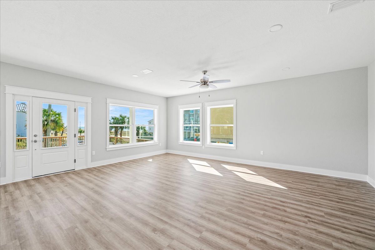 Wood flooring, white double doors with glass panes, ceiling fan with light, window with white frame, light reflecting on wooden floor