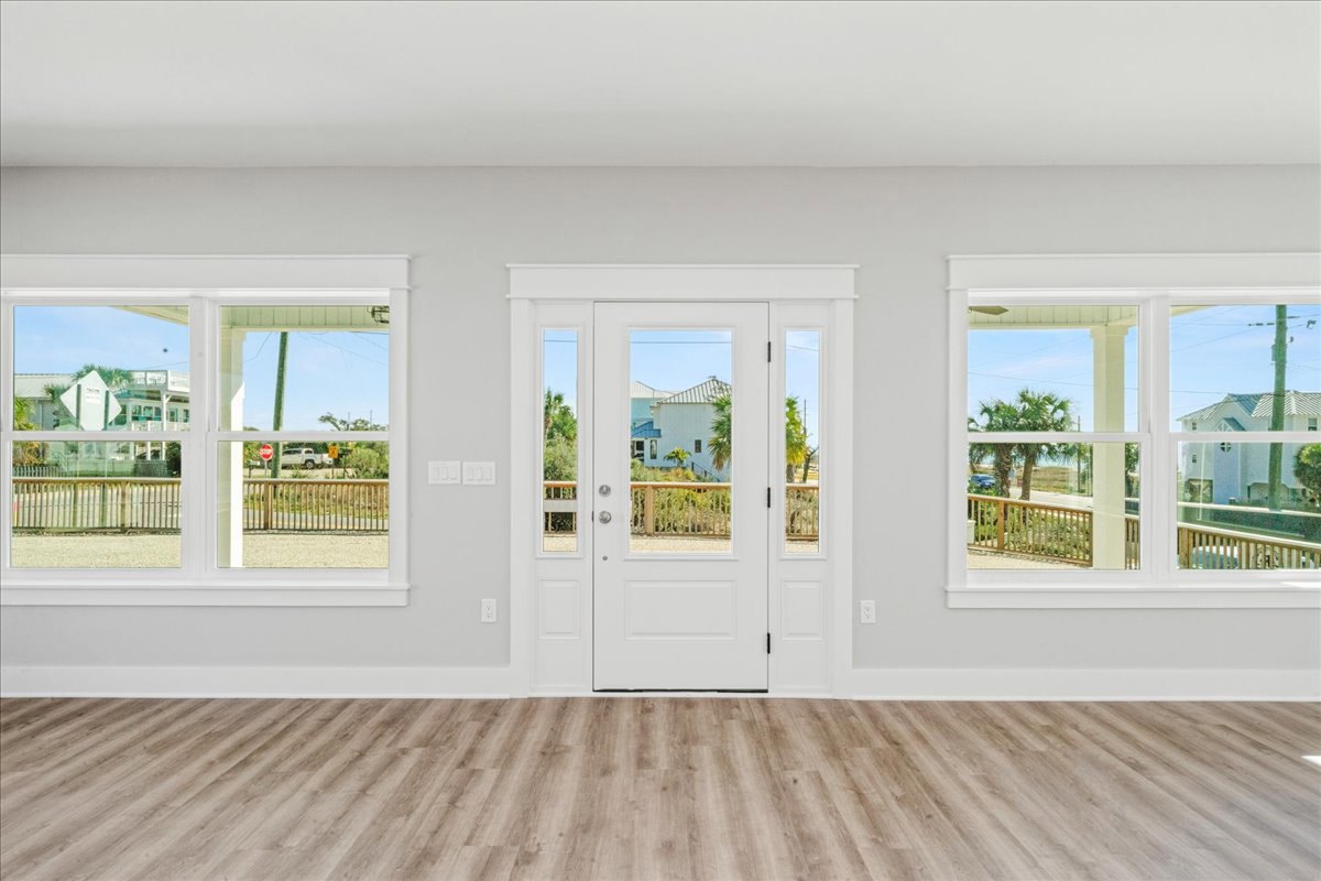 Bright room with white walls, large windows, wood flooring, and a white door featuring glass panes; view of neighboring house and fence visible through the window