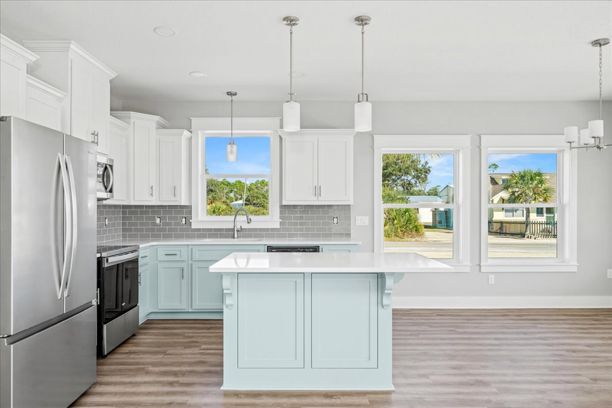 White kitchen with shaker cabinets, central island, stainless steel sink and faucet, black refrigerator with silver handle, light countertops, and hardwood flooring