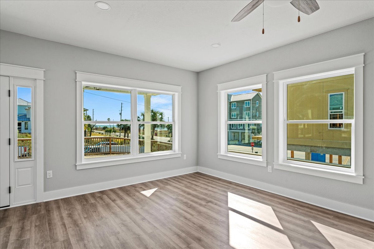 Spacious room featuring large windows with ocean and deck views, blue door, wood laminate flooring, white ceiling fan, and modern ceiling light fixture.