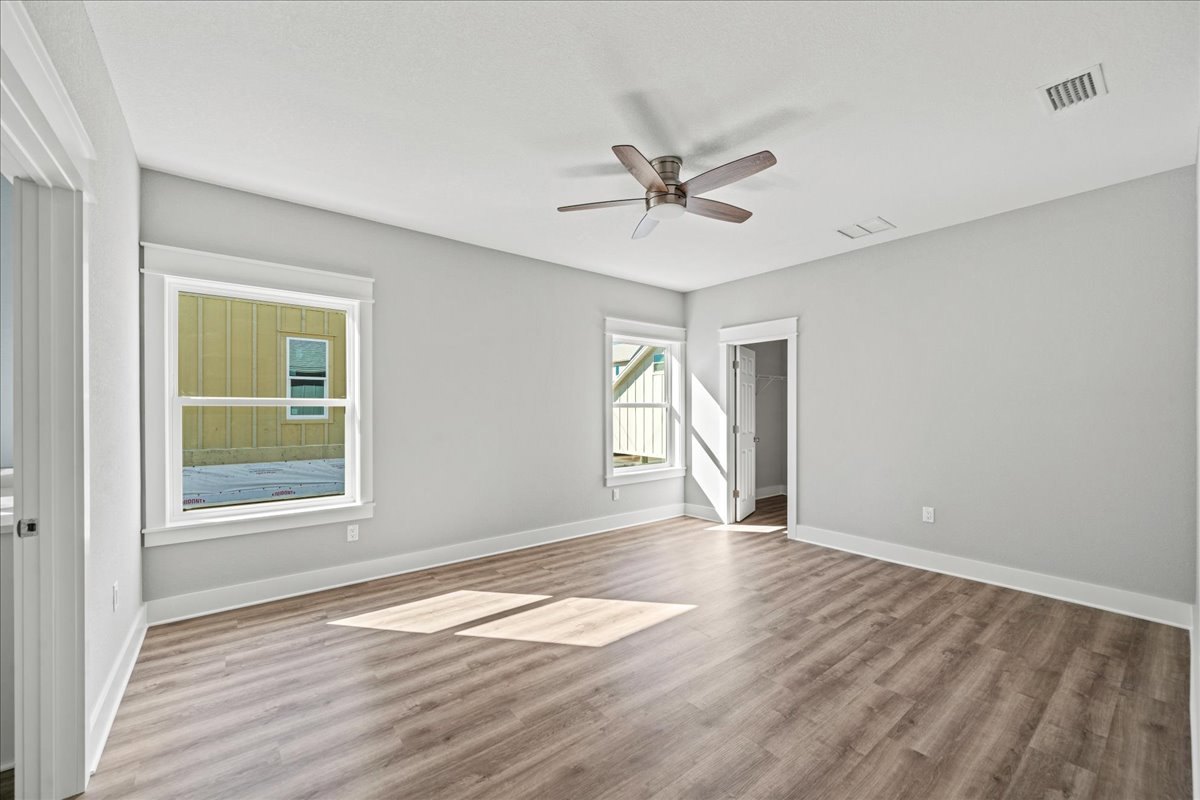 Wood flooring with sunlight streaming in, white-framed window, ceiling fan with light fixture, white door and railing, neutral walls