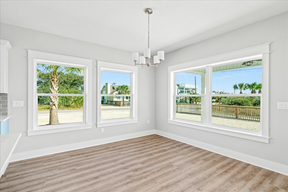 Spacious room with large windows, wood flooring, hanging light fixture, palm tree and neighboring house visible through windows, window blinds partially drawn