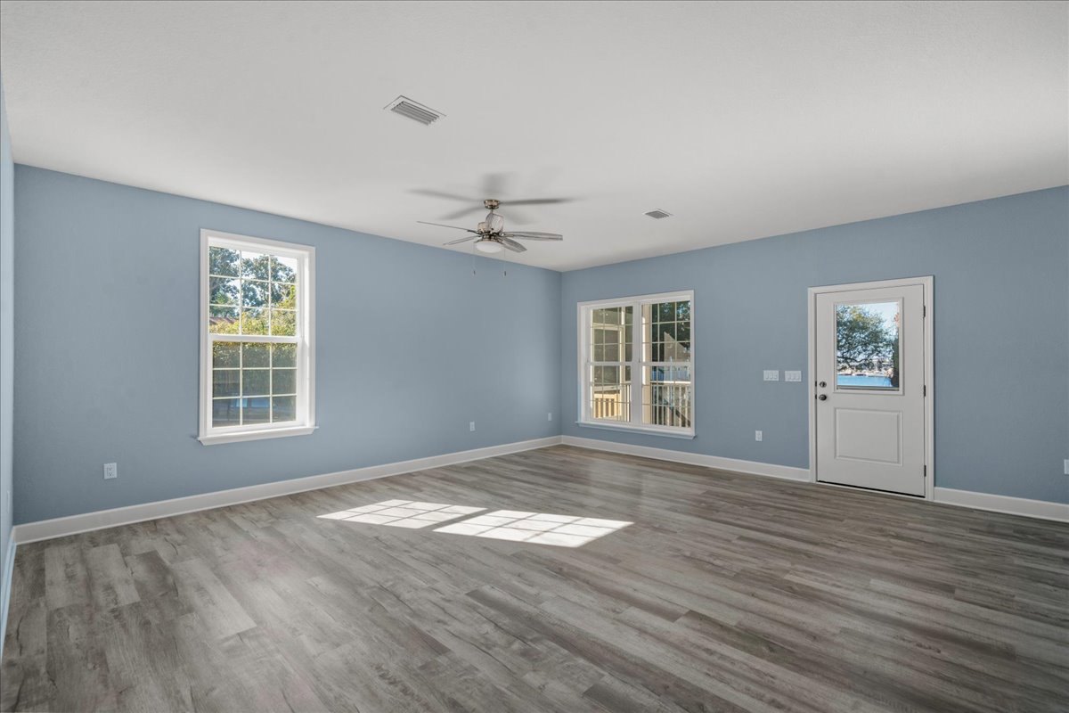 Room with wood flooring, white walls, white door with glass panel, large window with white frame, ceiling fan with light fixture