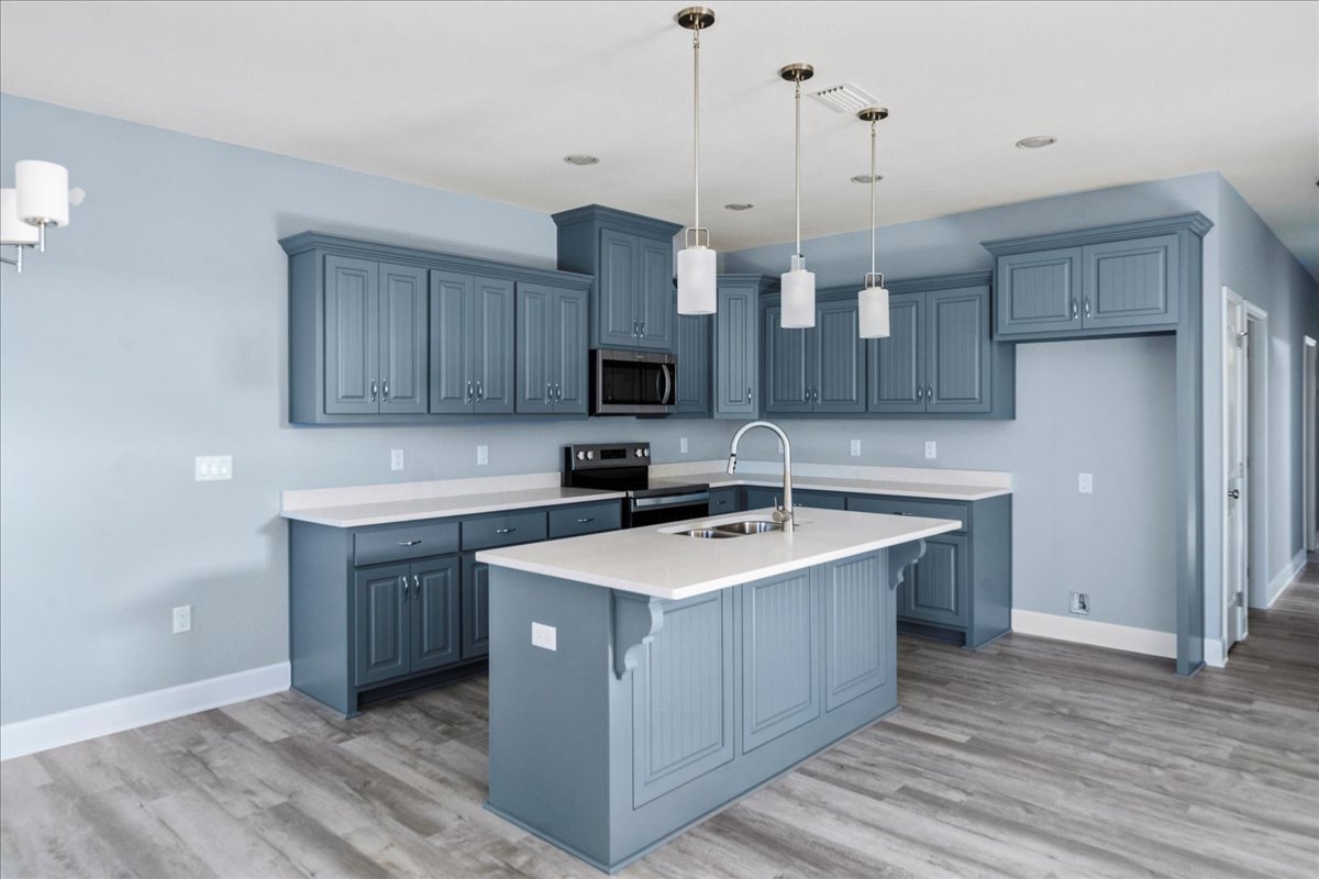 Spacious kitchen featuring a large central island with built-in sink and white faucet, open microwave oven, white lamp shade, and light-colored cabinetry with drawers and