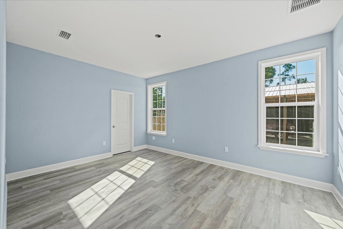 Light blue walls, white-framed window, white door with silver knob, wood laminate flooring illuminated by sunlight.