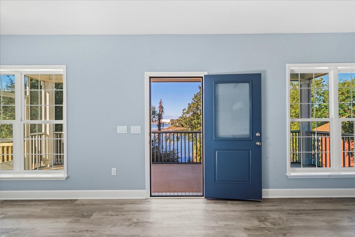 Blue door with glass panels, wood floor, large windows overlooking balcony with metal railing and trees, view of water in background