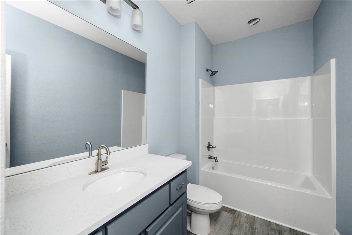 Modern bathroom featuring a white bathtub, wall-mounted sink with chrome faucet, white toilet, large mirror, and light gray tile walls
