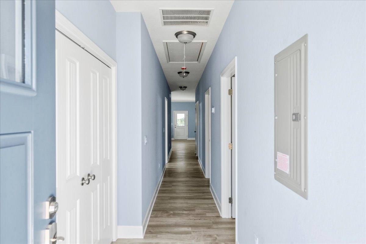 Long hallway with light blue walls, wood flooring, multiple white doors including one with a window and one with a lock, ceiling vent visible
