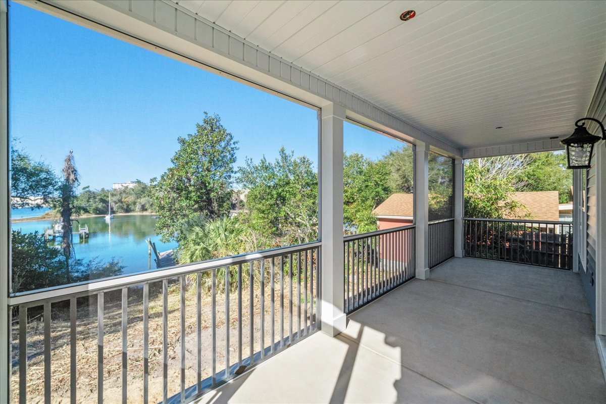 Wood deck with metal railing, concrete floor, shaded by nearby trees, overlooking a calm lake and blue sky.