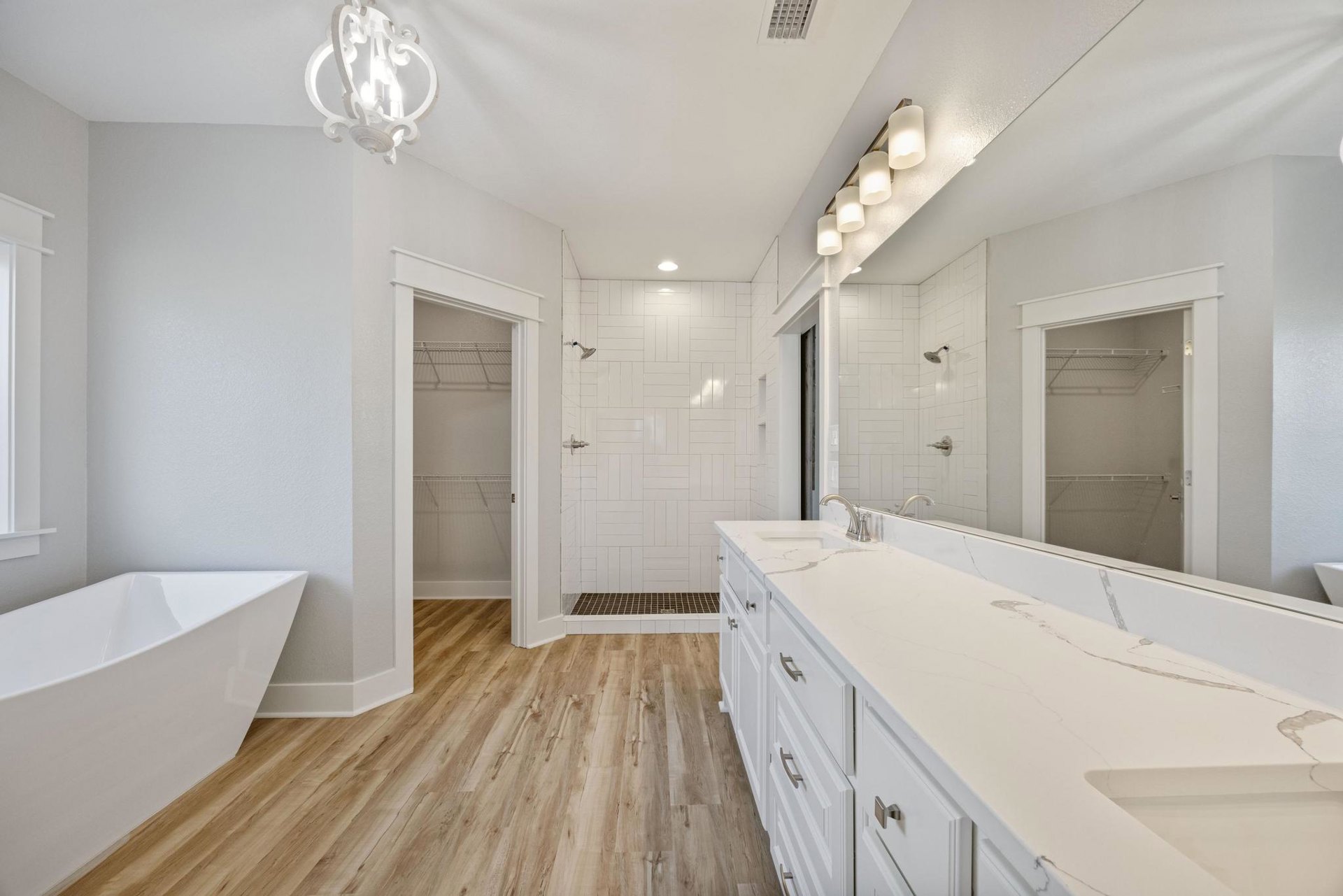 Bathroom with white freestanding tub, white countertop sink, large wall mirror, open shelving behind door, and modern light fixture against tiled walls