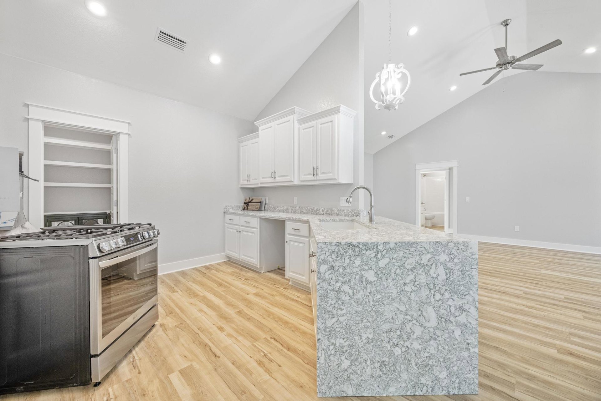 Spacious kitchen featuring a large central island with grey cabinetry, white quartz countertops, stainless steel stove and oven, modern ceiling fan with integrated light, and sleek