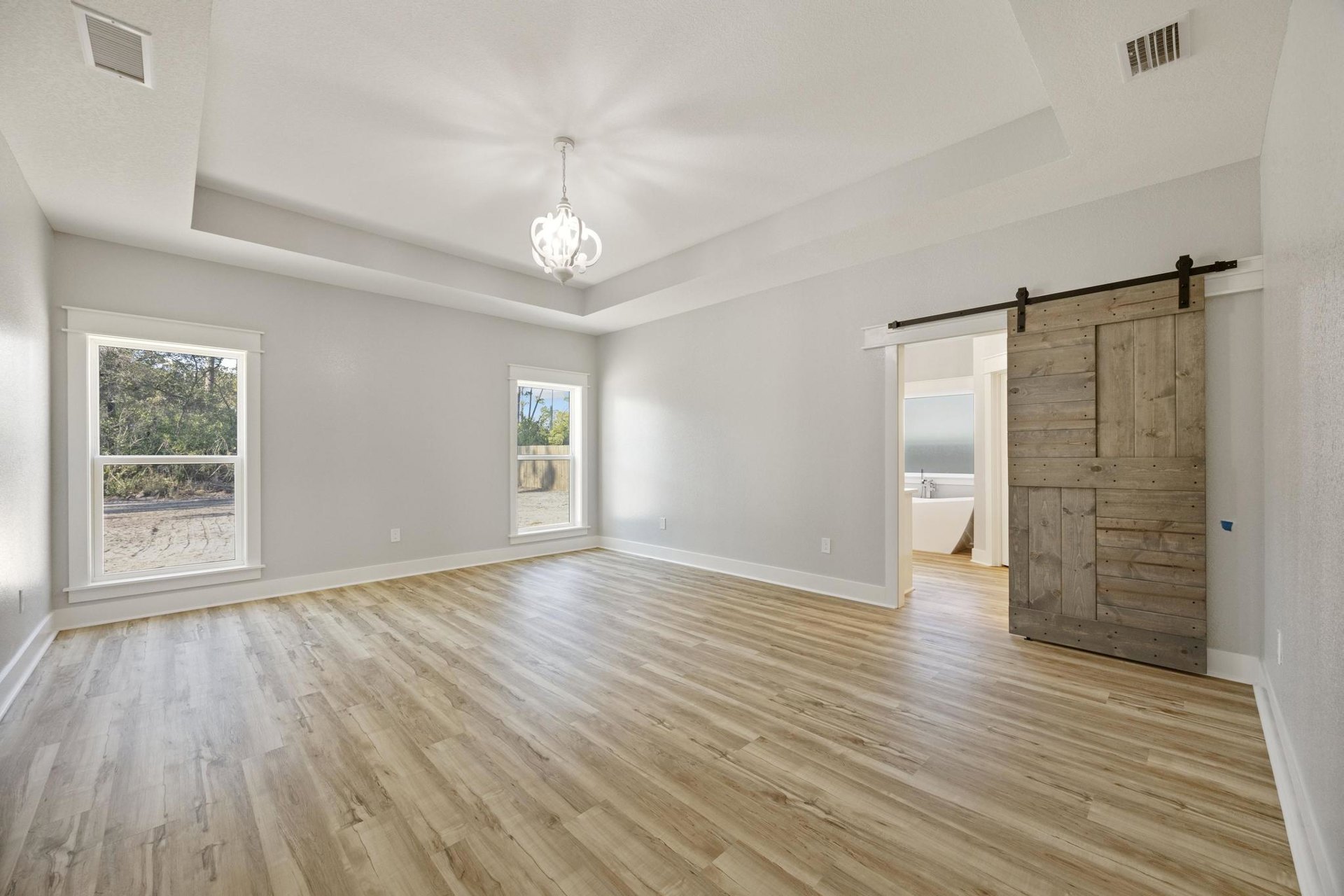 Wood-floored room featuring a sliding barn door, chain-hung light fixture, plaster walls, and windows overlooking trees and a fence; close-up of wood panel detail visible.