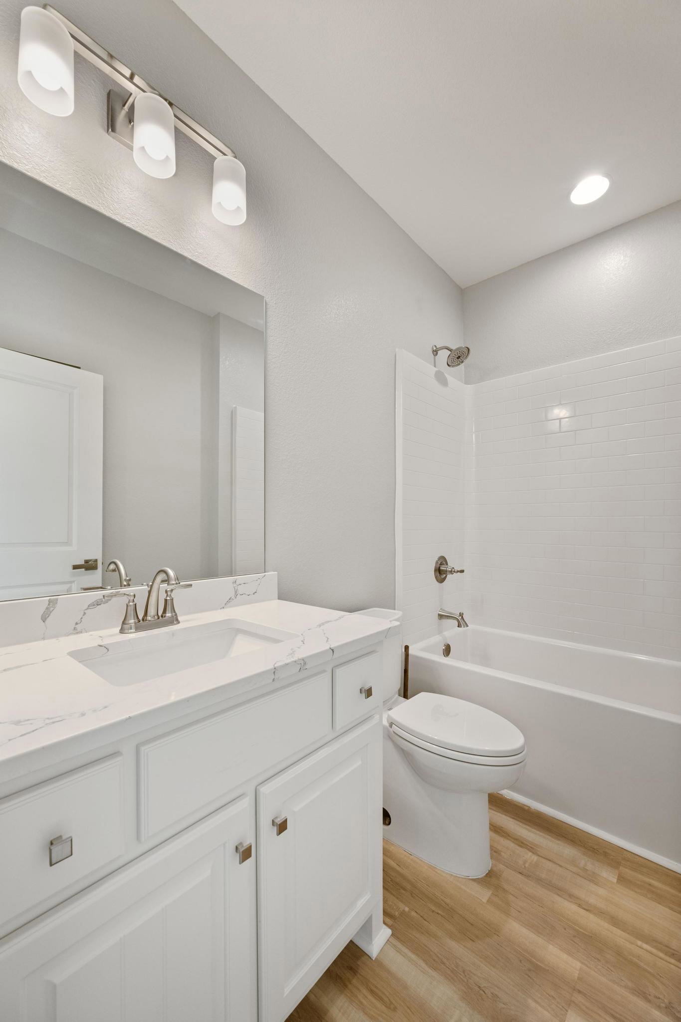 Bathroom with white toilet, built-in bathtub, light-colored tile walls, overhead ceiling light, and white vanity cabinet