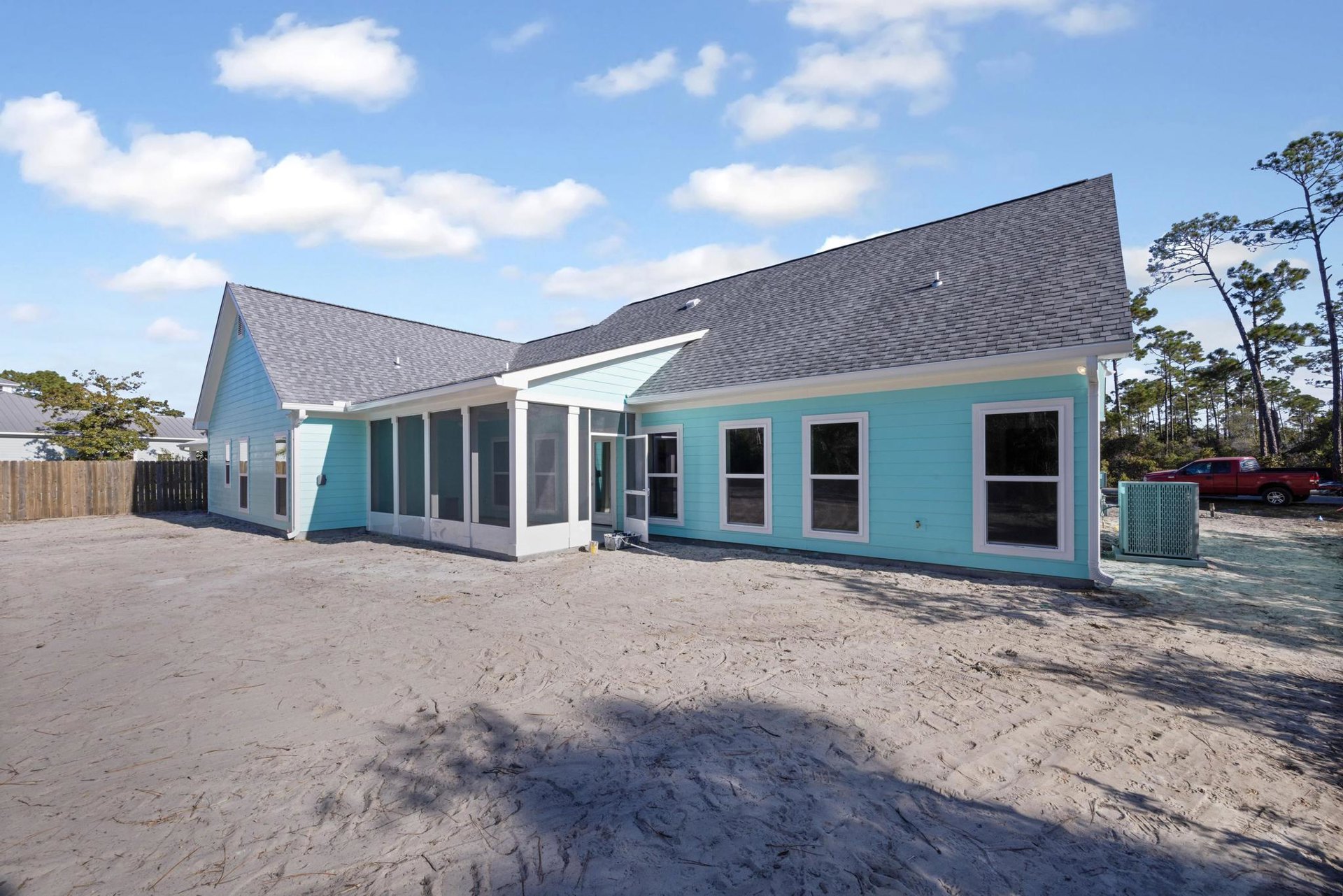 Blue house with white trim and window frames, expansive grassy yard, red truck parked on roadside, person near white fence, trees and clouds in background