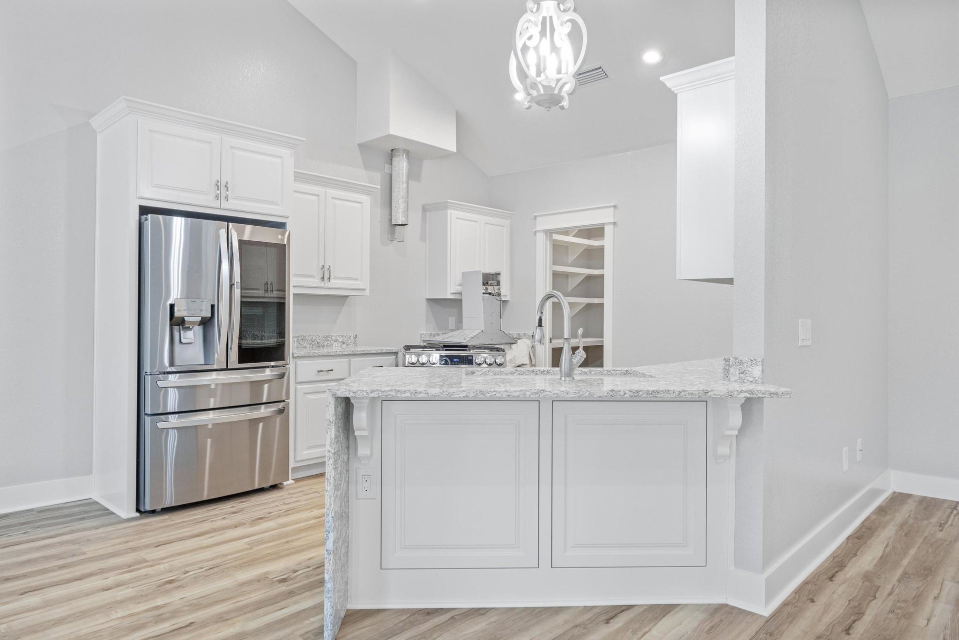 Spacious kitchen featuring a large white island with built-in sink, stainless steel refrigerator with ice and water dispenser, stainless steel stove, white cabinetry with square