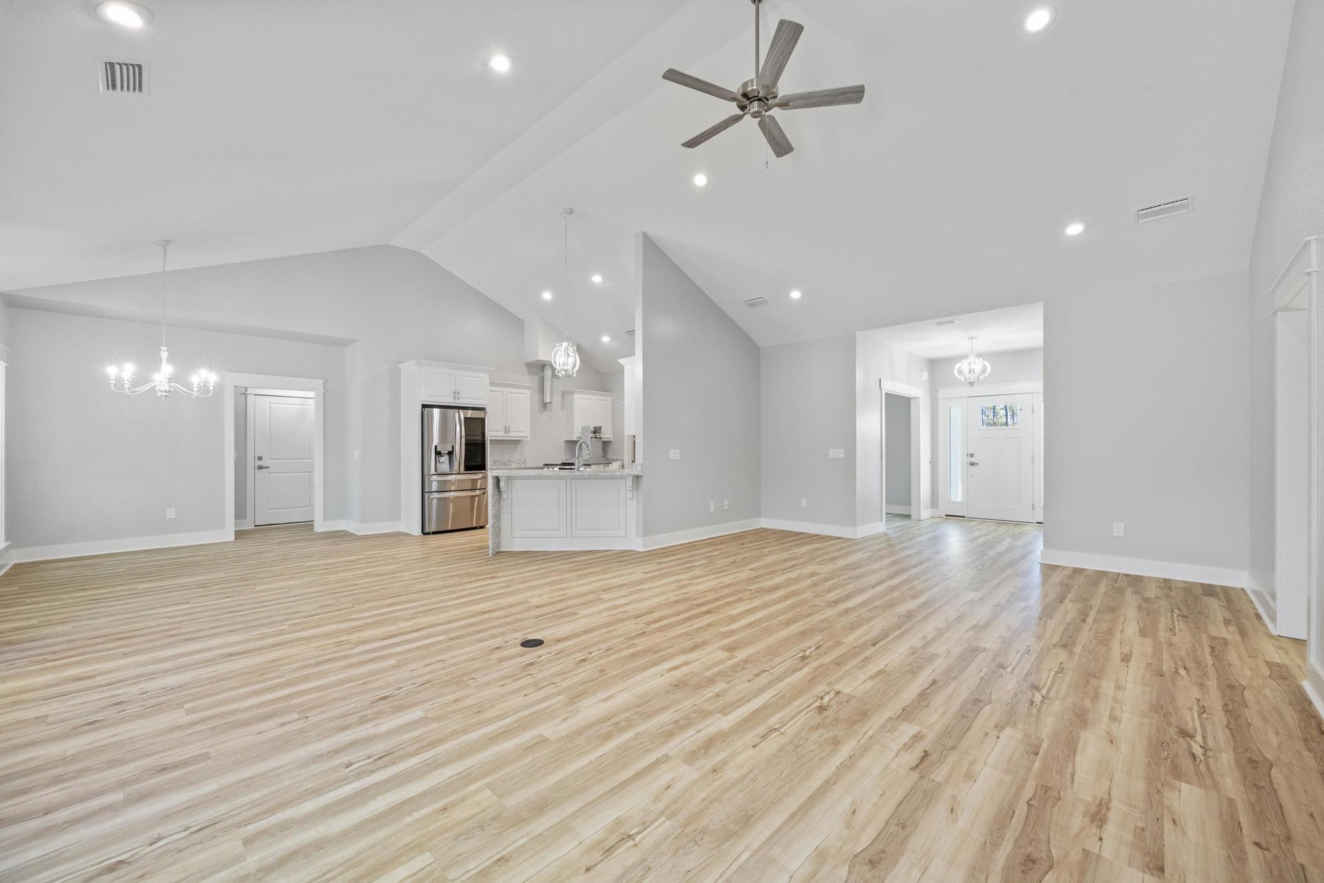 Spacious room with wood flooring, white walls, ceiling fan with wood blades, white door with window, stainless steel refrigerator