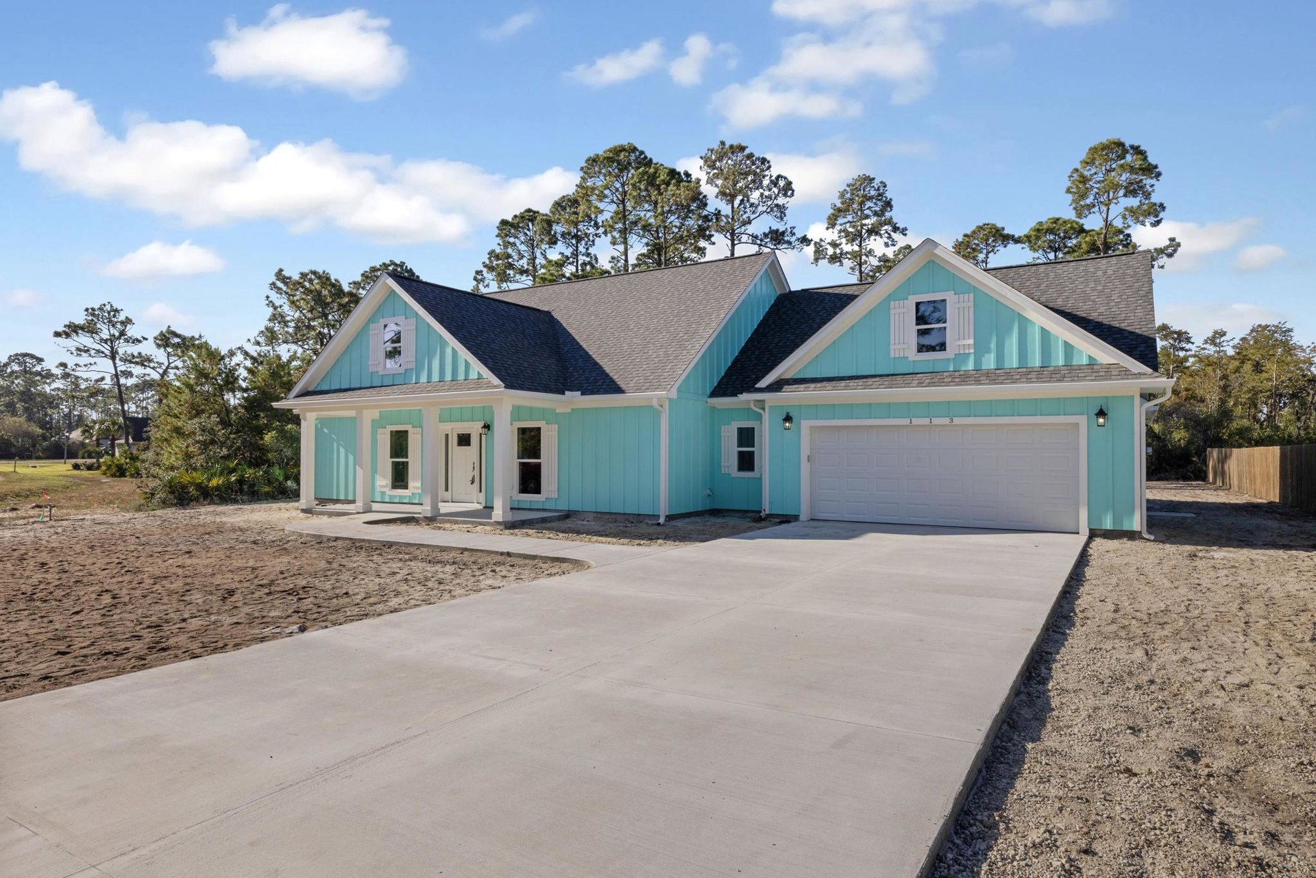 Blue siding house with white front door, concrete driveway, white garage door, green accent wall, and white-trimmed windows under partly cloudy sky