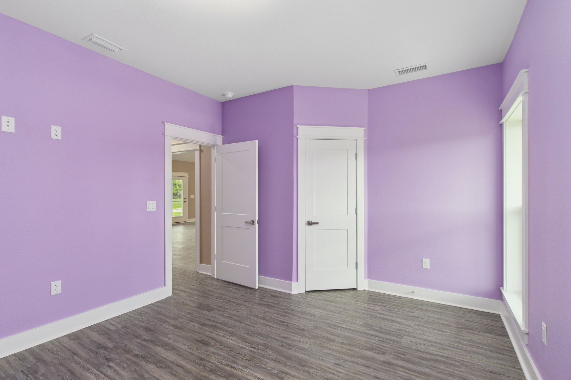 Purple-painted walls and doors, white door with silver handle, wood laminate flooring, white electrical switches on purple wall, white surface with black spot, close-up of window.