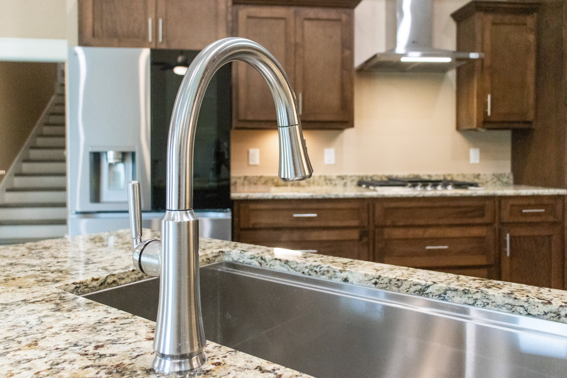 Stainless steel kitchen sink with chrome faucet set in a sleek countertop, white tile backsplash visible in background