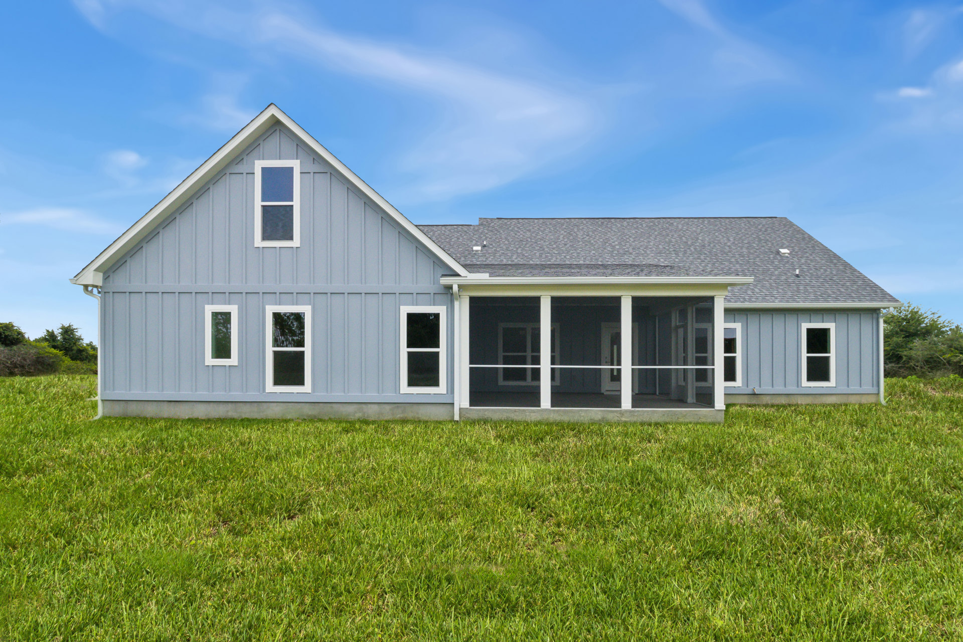 White farmhouse-style home with two covered porches, black screened windows, blue window trim, manicured grass lawn, and trees visible outside under a clear blue sky.