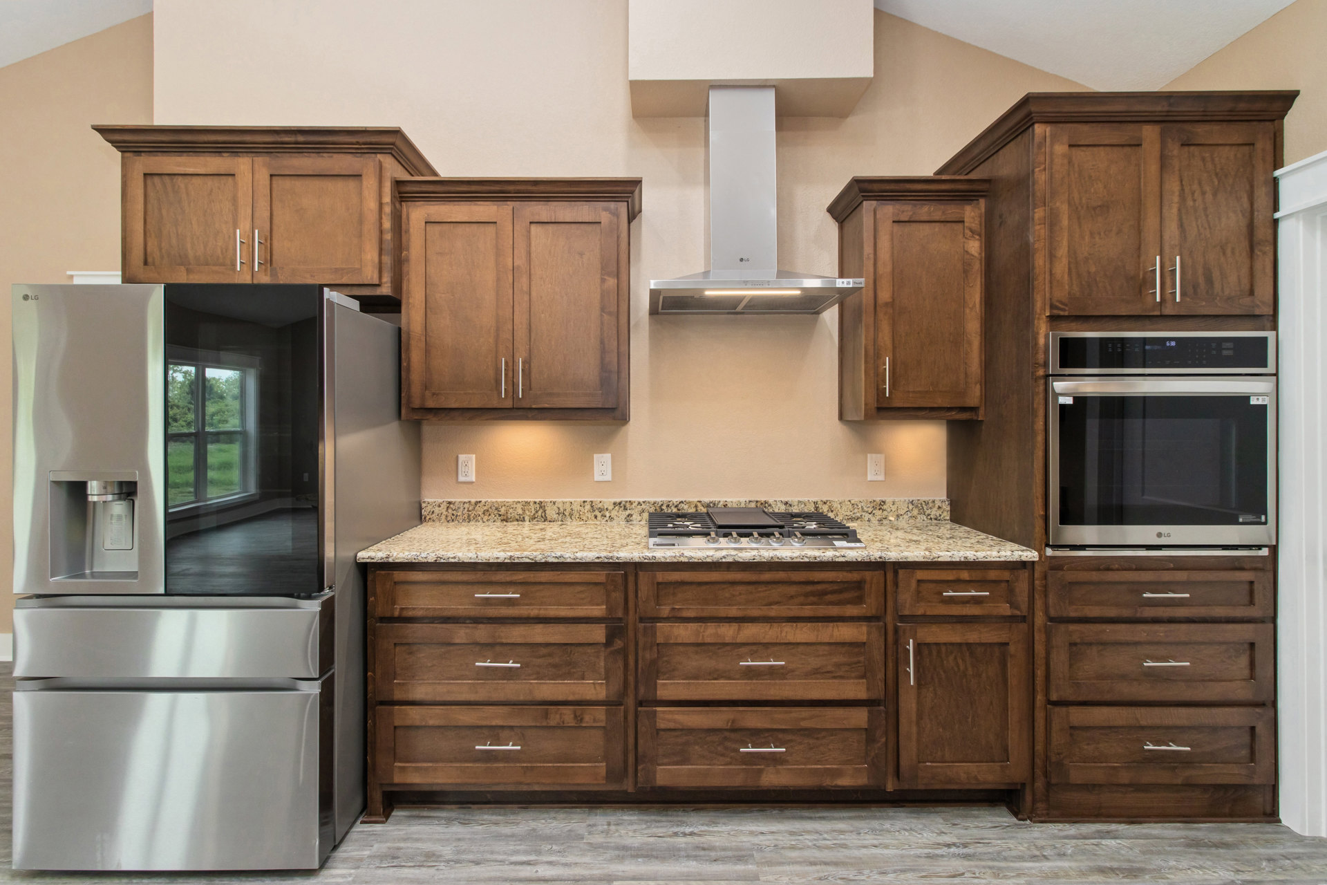 Kitchen with wooden cabinets, stainless steel refrigerator with glass door, microwave oven, stove top on stone countertop, and drawers with metal handles