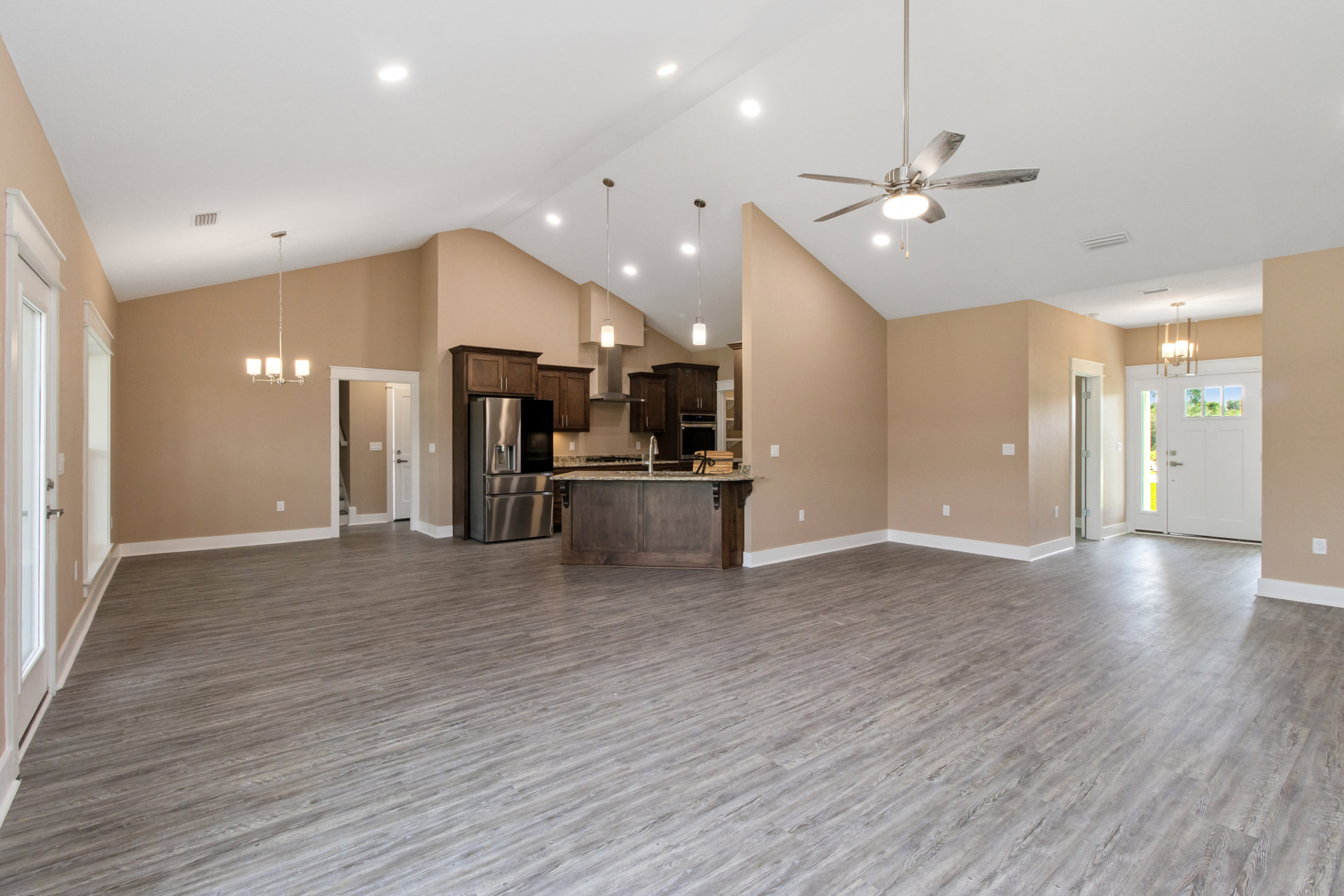 Open floor plan featuring wood flooring, kitchen island with built-in sink and stove, stainless steel refrigerator with black glass door, ceiling fan with light, and door with