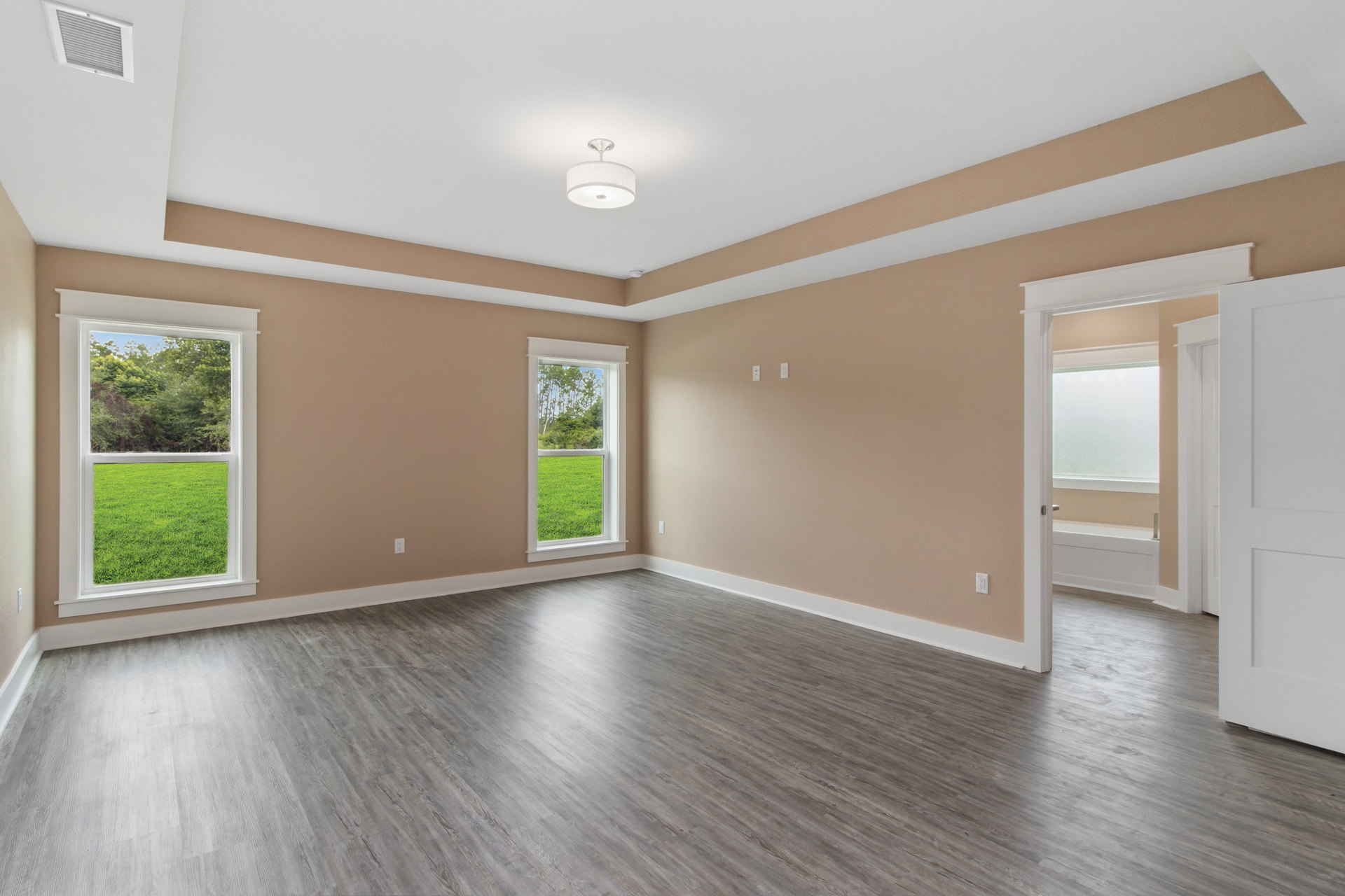 Spacious room featuring large windows overlooking a green grass field, light wood flooring, white walls with plaster finish, and a modern white ceiling light fixture.