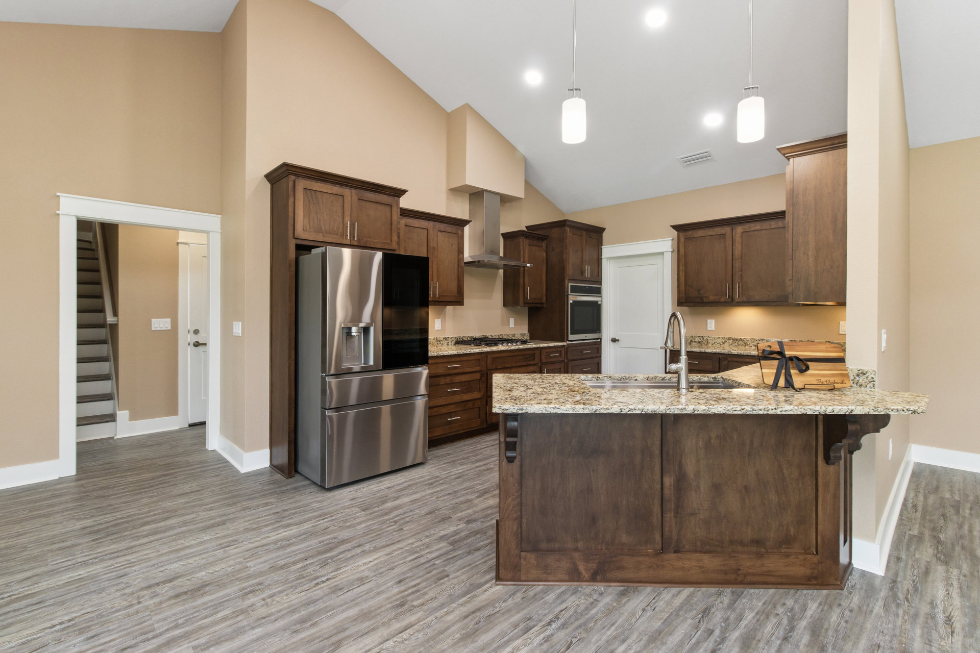 Kitchen with granite countertops, large central island, stainless steel refrigerator with water dispenser, tile flooring, white cabinetry, built-in microwave, and sink on the