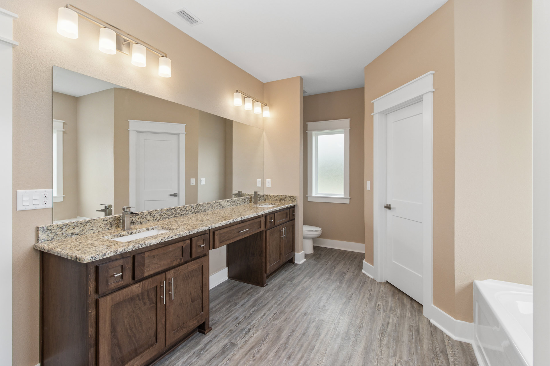 Bathroom with marble countertop, white toilet, white bathtub with glass door, frosted glass window, white cabinetry, silver door handle, and tiled floor.