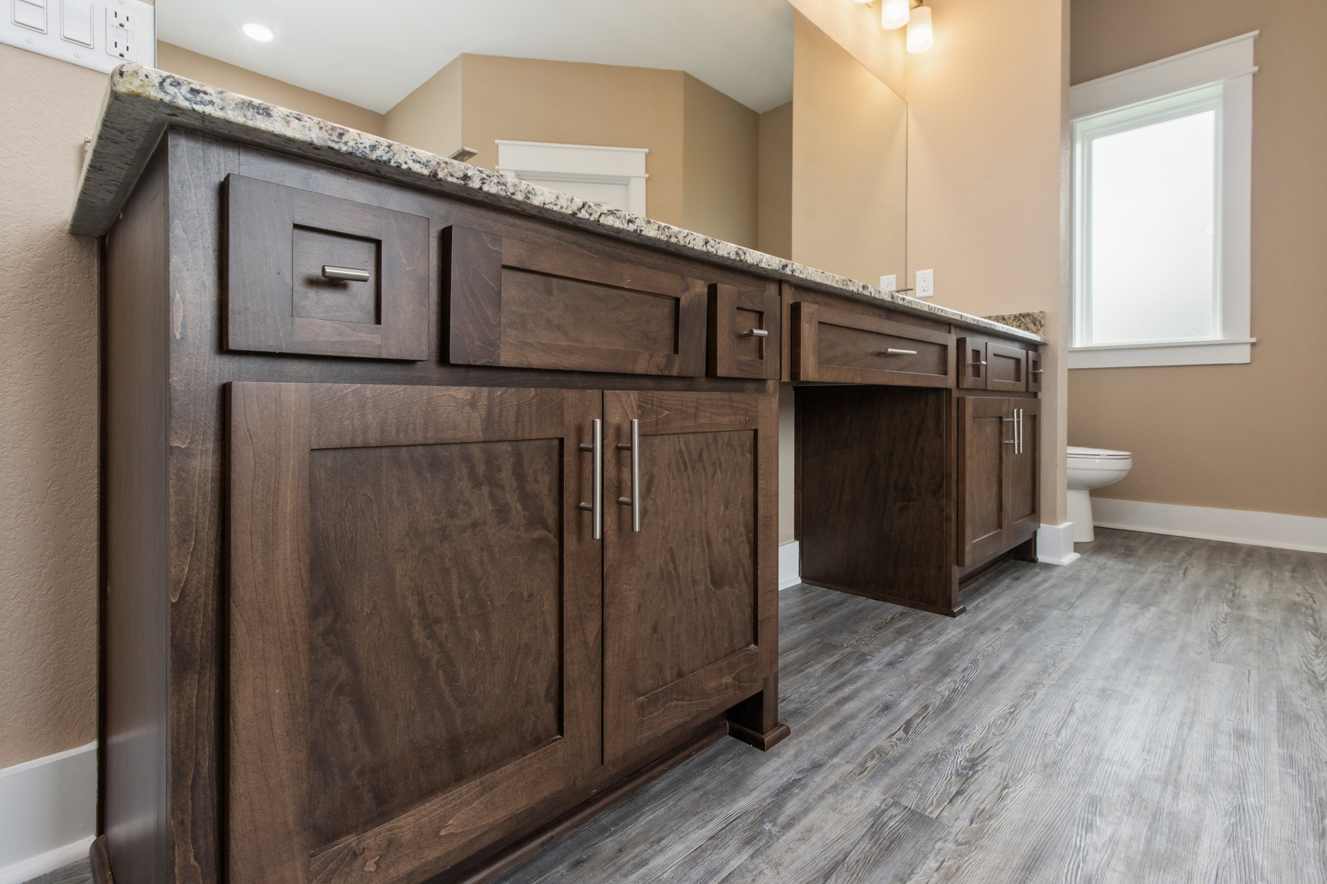 Bathroom with marble countertop, white framed rectangular window, wood flooring with white baseboards, white toilet, and cabinetry with marble surface