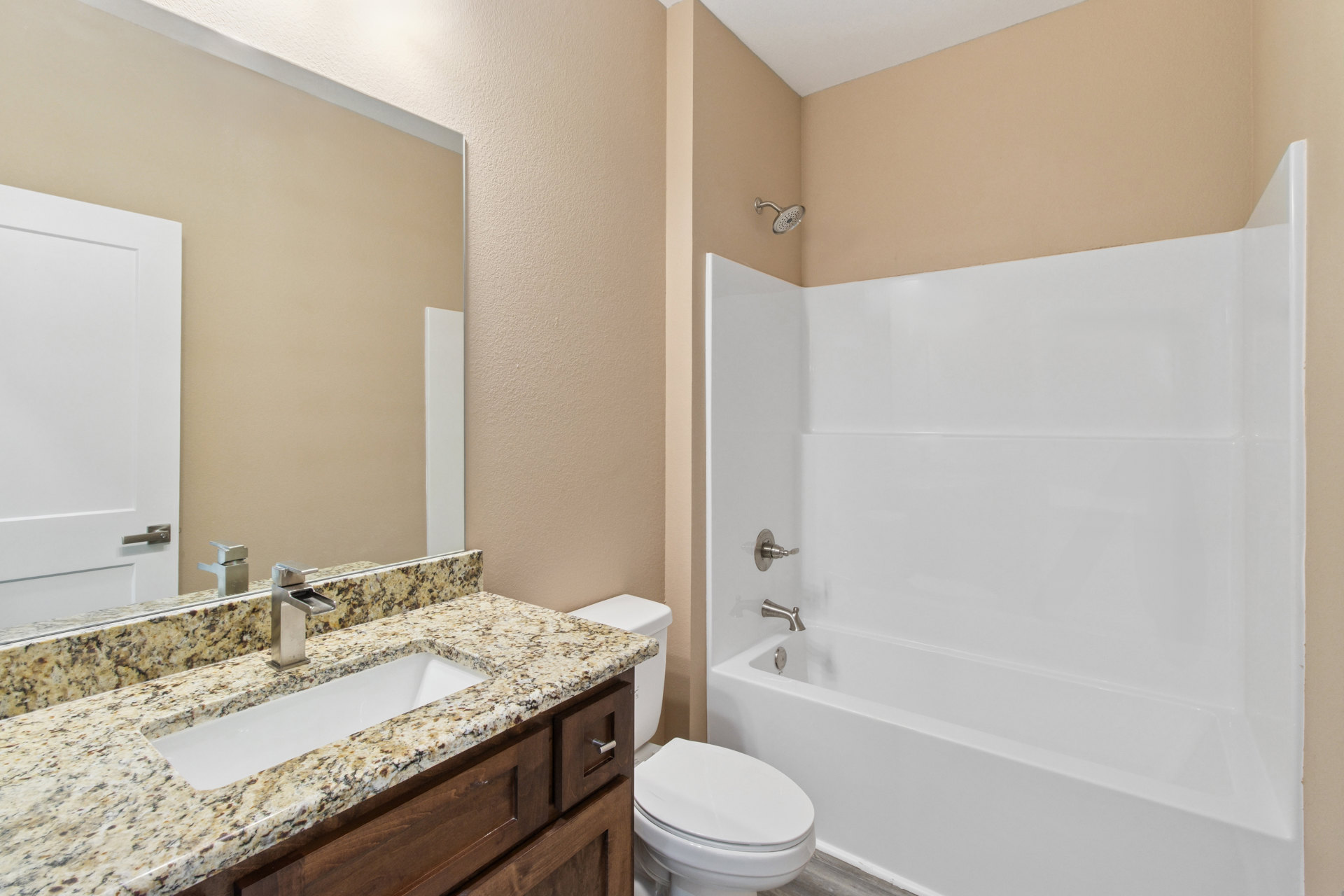 Bathroom with white toilet, rectangular sink and chrome faucet on marble countertop, metal towel bar, white bathtub, tile flooring, white walls with brown trim