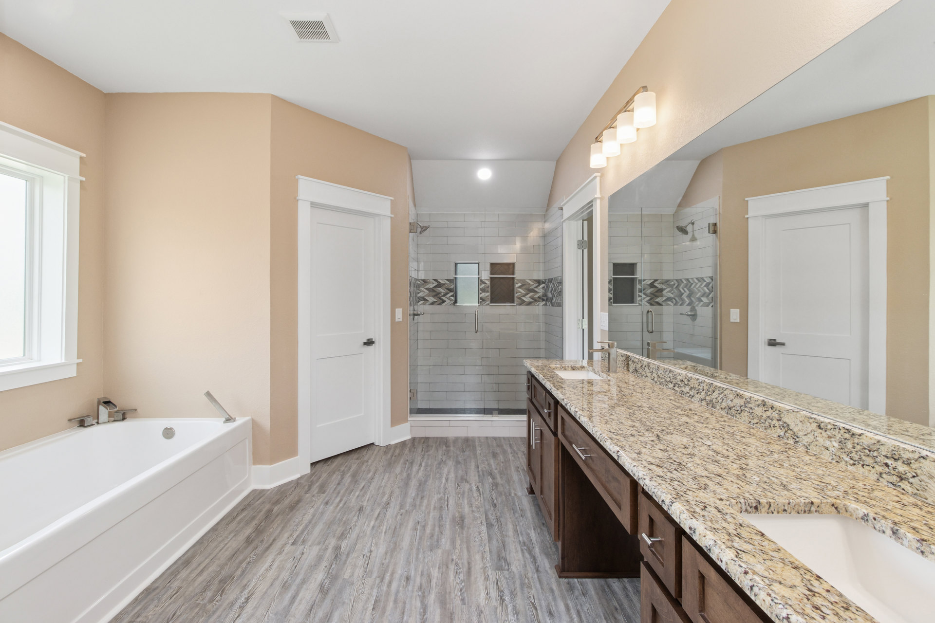 Bathroom featuring a marble countertop with dual sinks, freestanding bathtub with chrome faucet, wood flooring, tiled shower enclosure, and white paneled door