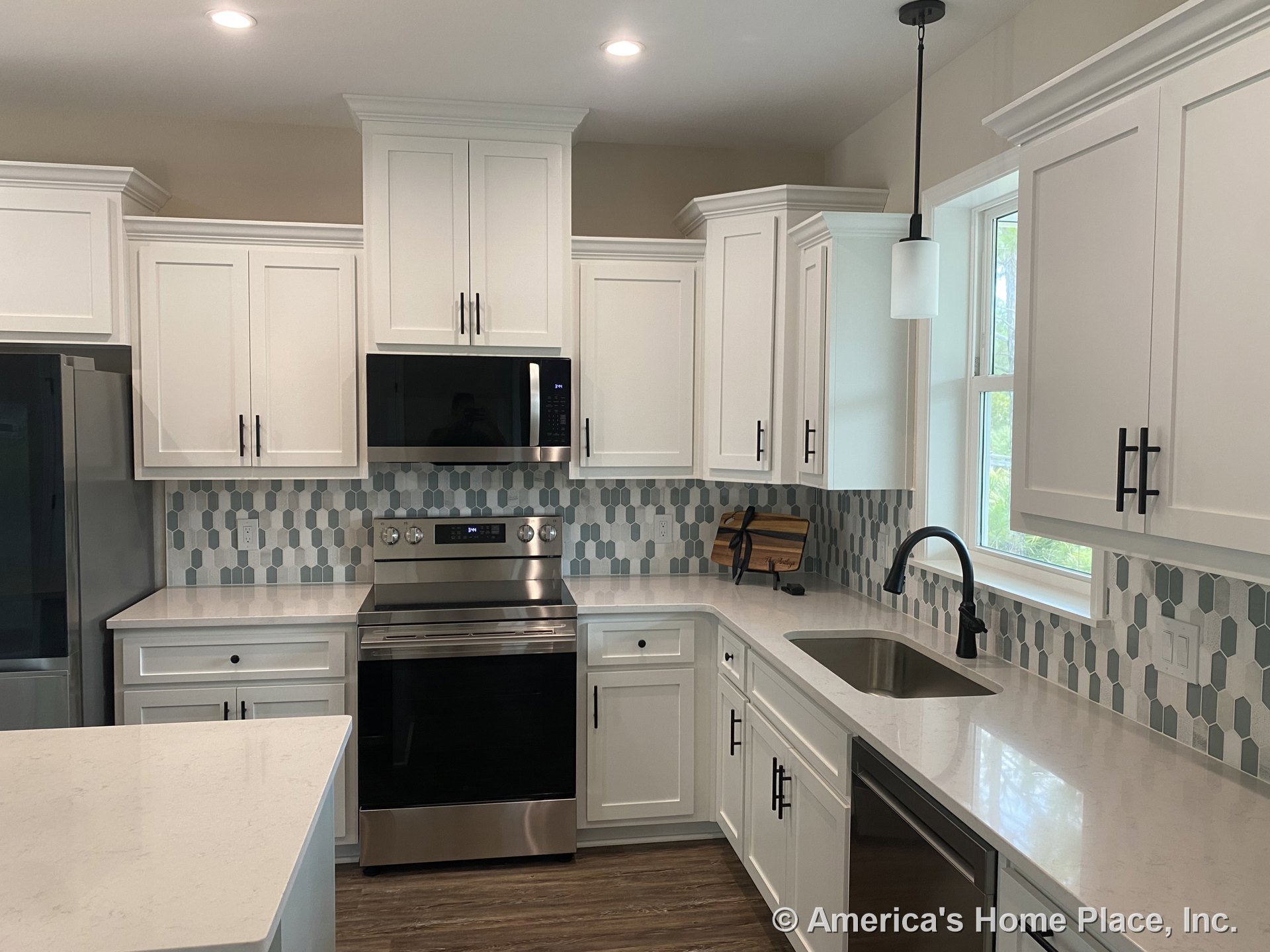 White shaker cabinets with quartz countertops, hexagonal tile backsplash, stainless steel appliances including built-in microwave and electric range, undermount sink with