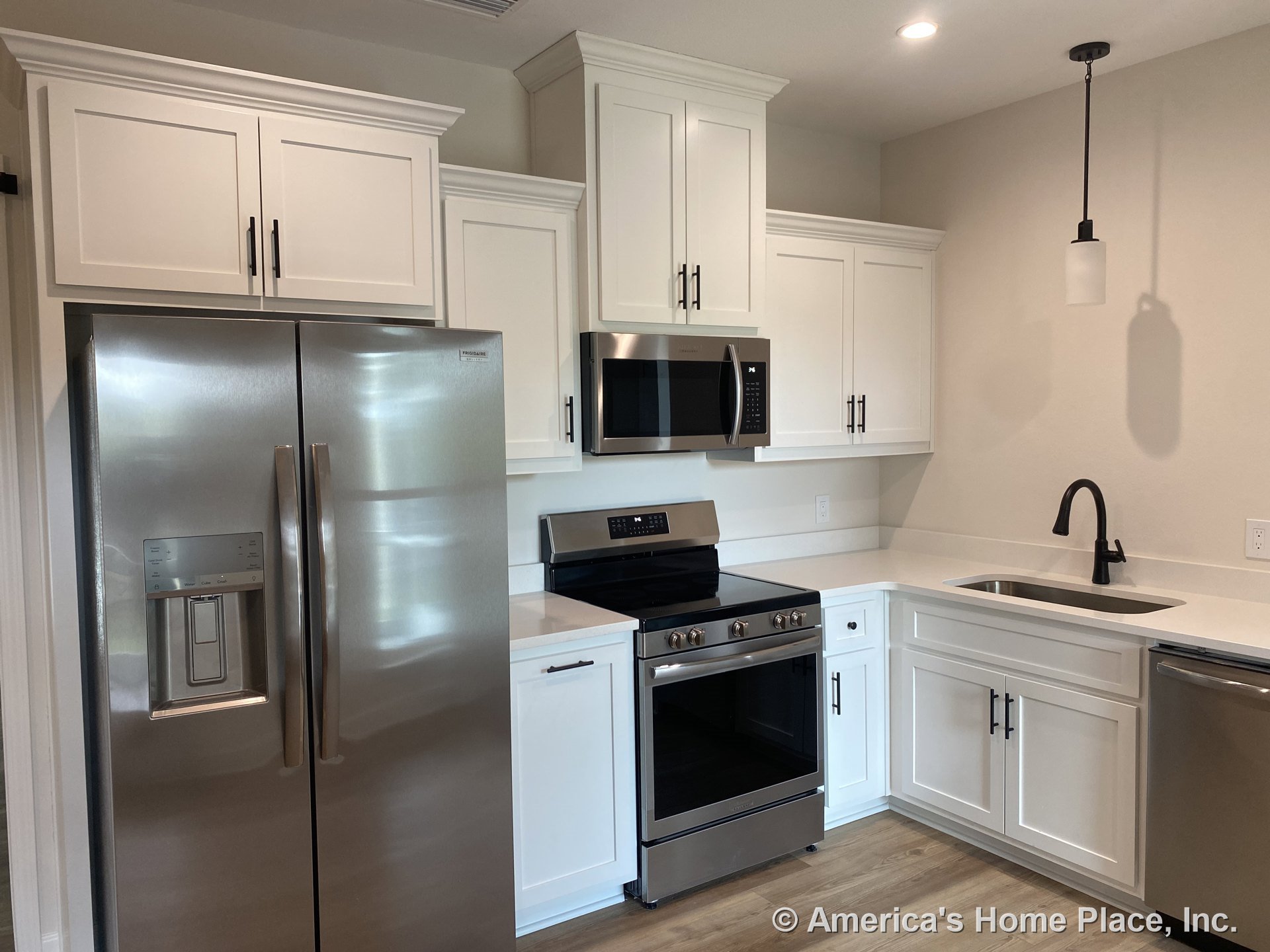 White shaker cabinets with stainless steel refrigerator, built-in microwave above electric range, quartz countertops, single bowl undermount sink with modern faucet, pendant